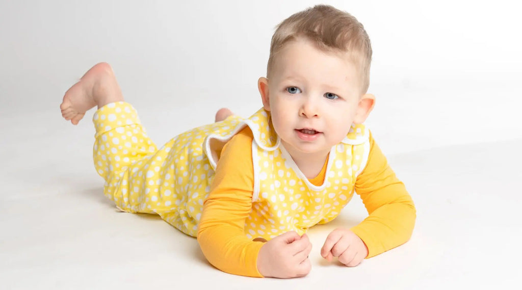 Szőke kisfiú sárga liaabébé tipegá háózsákban hasal és nagyon cuki