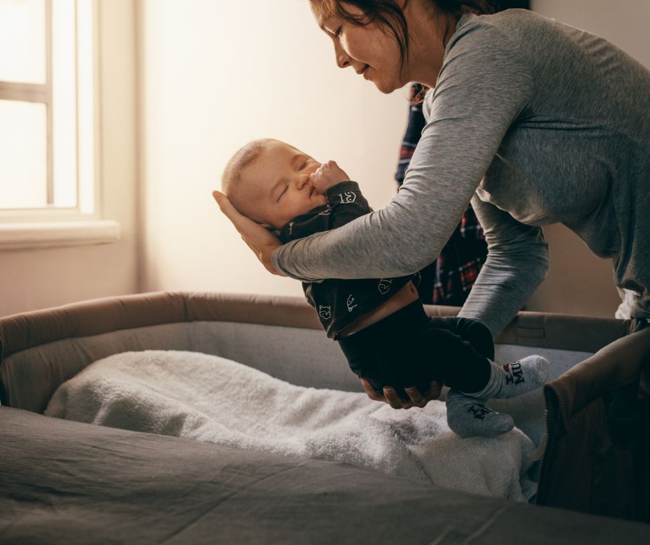 Egy édesanya gyengéden, szeretettel teszi be alvó kisbabáját a kiságyba.