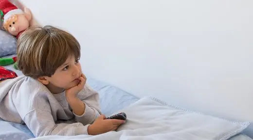 kisfiú hasal távkapcsolóval a kezében az ágyon