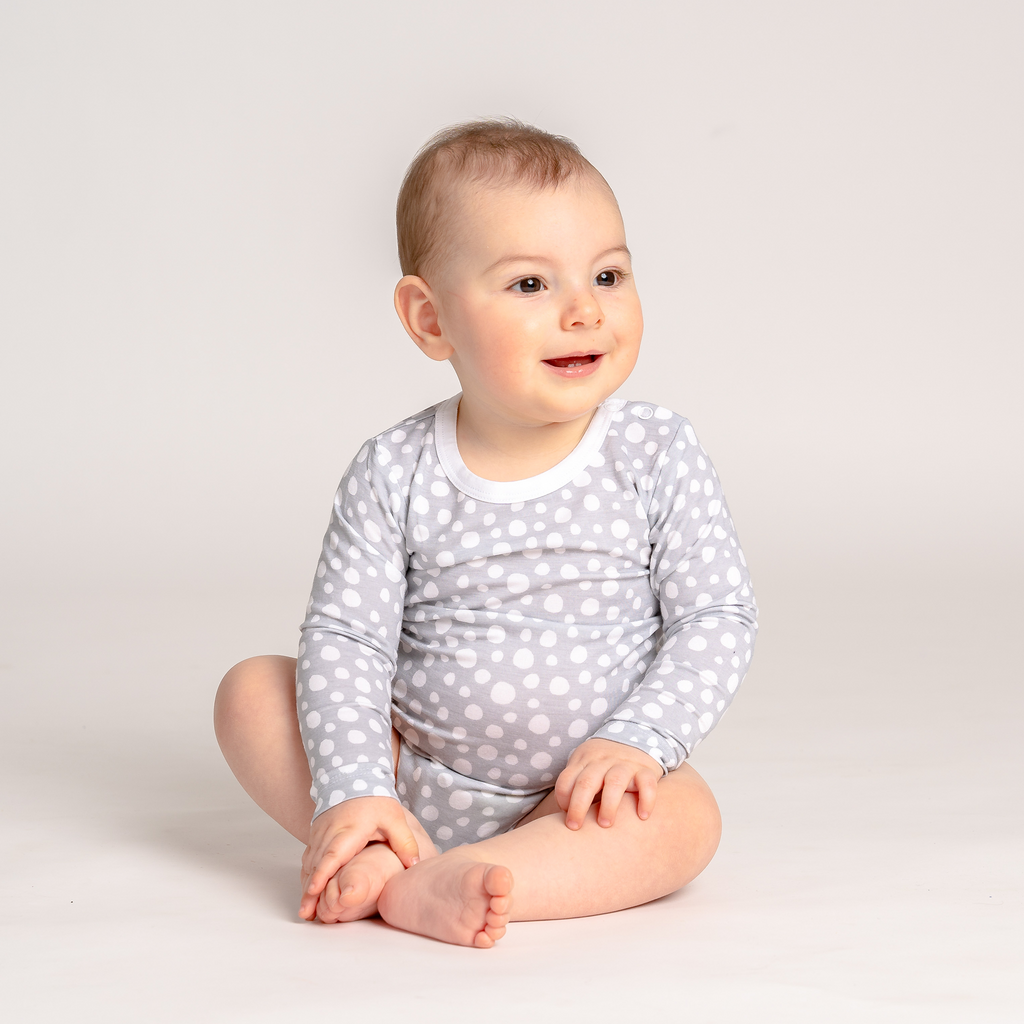 Smiling baby girl playing in LiaaBébé toddler long sleeve bodysuit in Light Grey color with dots.