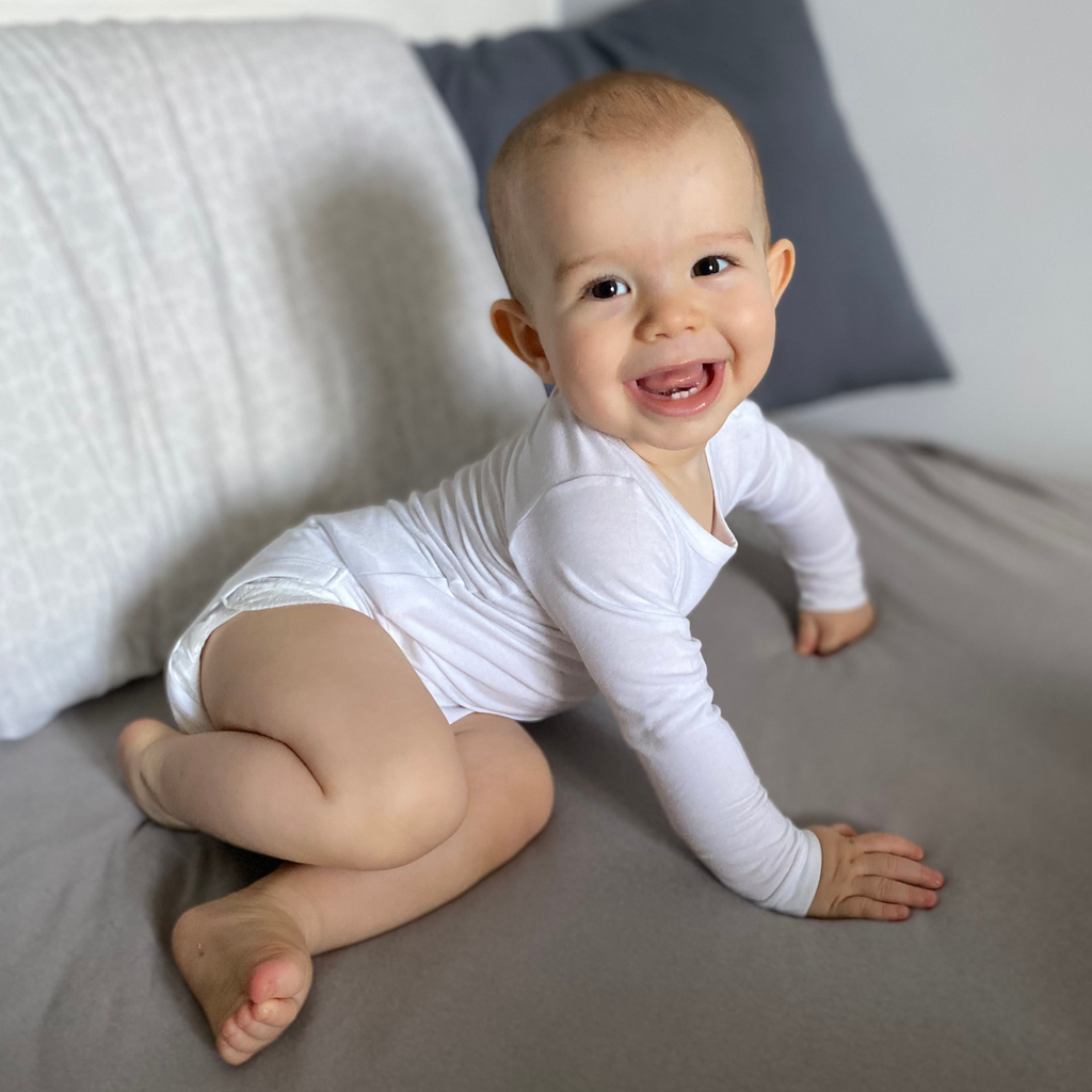 Little smiling baby boy wearing white LiaaBébé Long Sleeve Bodysuit.