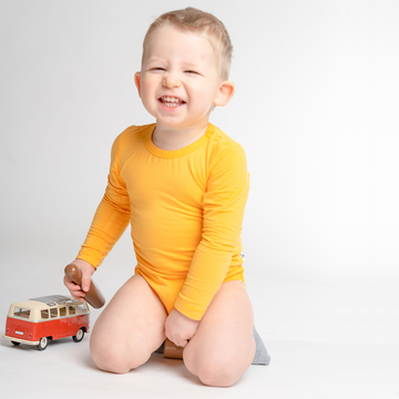 Smiling little boy wearing LiaaBébé Long Sleeve Bodysuit in marigold orange color.