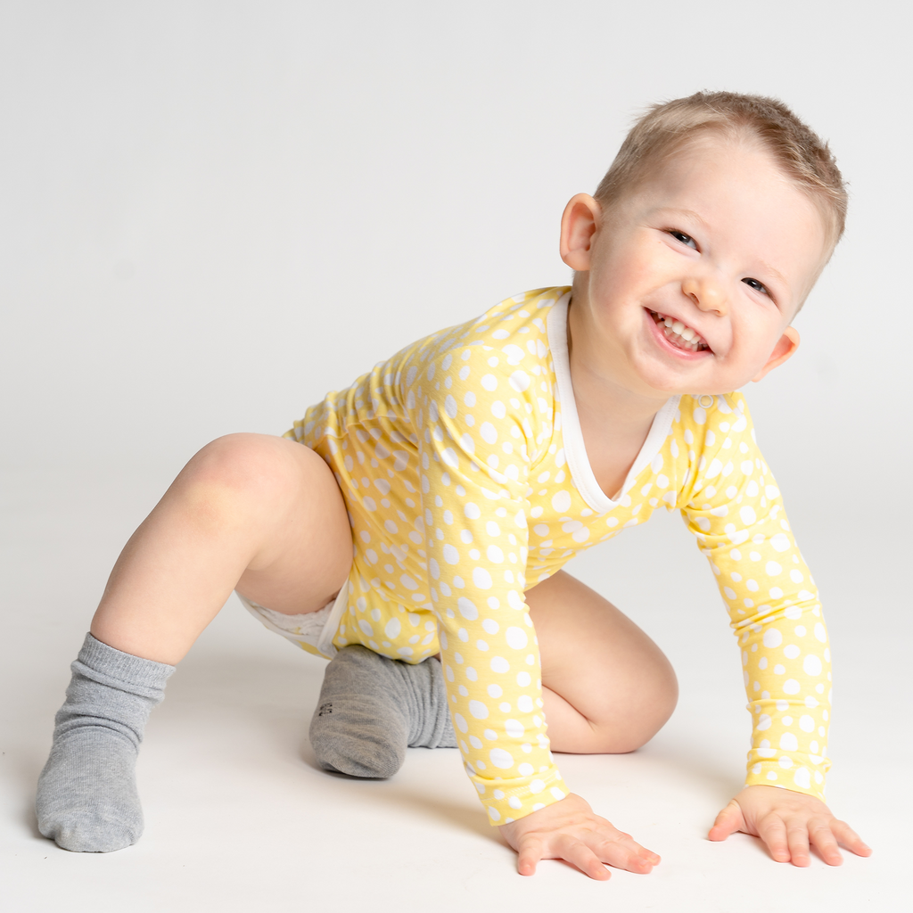 Smiling baby boy playing in LiaaBébé toddler long sleeve bodysuit in Light Yellow color with dots.