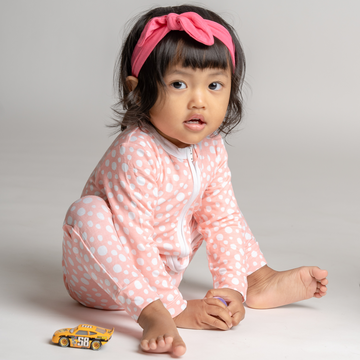 Little girl playing in LiaaBébé Top Knot Headband in hot pink color and in matching LiaaBébé Sleepsuit.