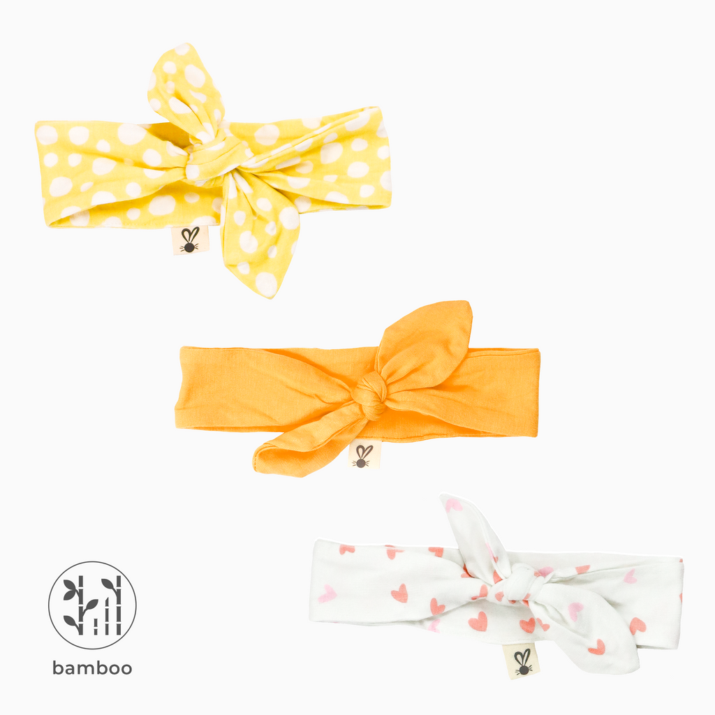 Three LiaaBébé Top Knot Headbands in marigold orange, light yellow with dots and one with pink hearts.