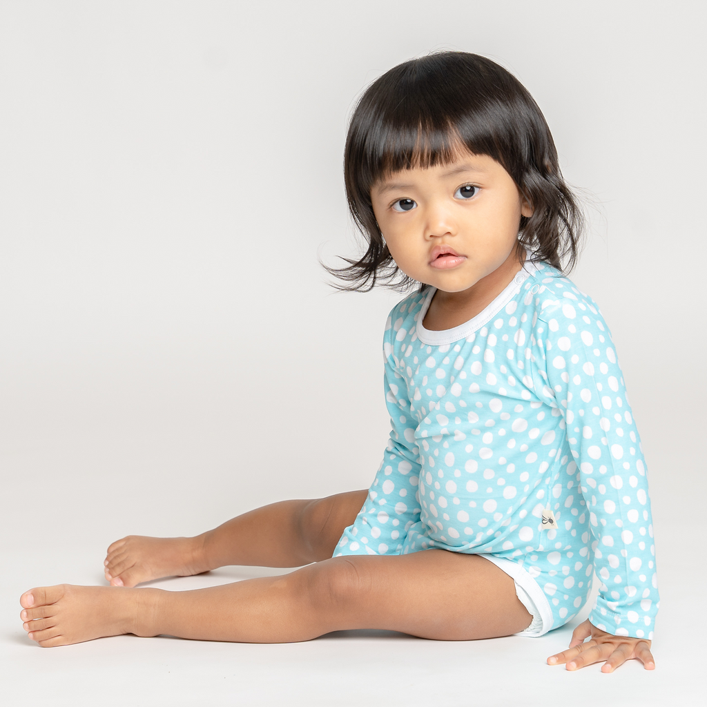 Little baby girl playing in LiaaBébé toddler long sleeve bodysuit in Light Blue color with dots.