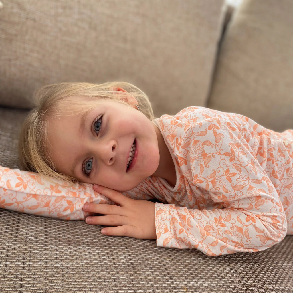 Szőke kislány mosolyogva fekszik a kanpén barackvirágos bambusz pizsamában