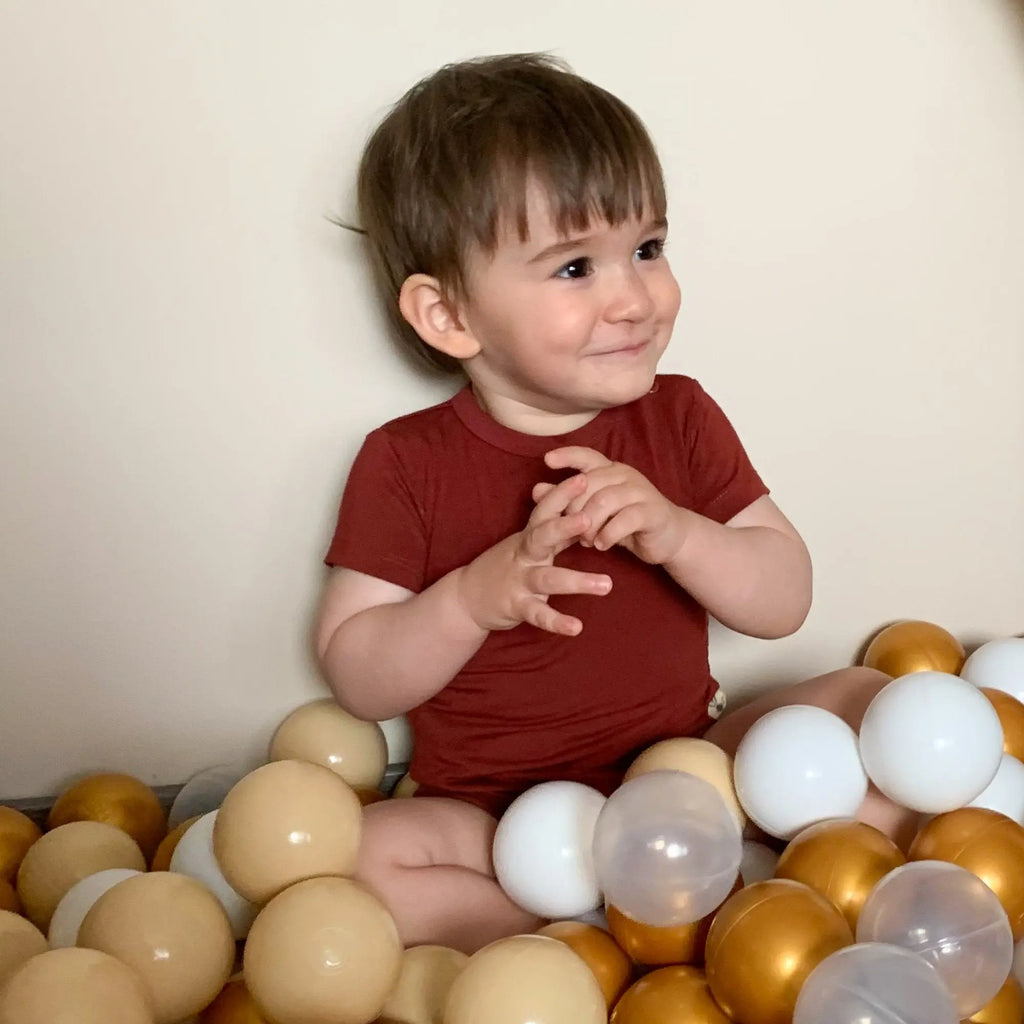 Kisifú barna bambusz bodyban labdák között ül