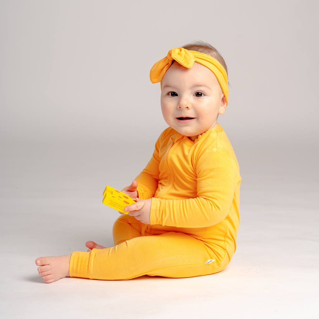 Smiling little girl sitting and playing in LiaaBébé Sleepsuit in Marigold Orange color.