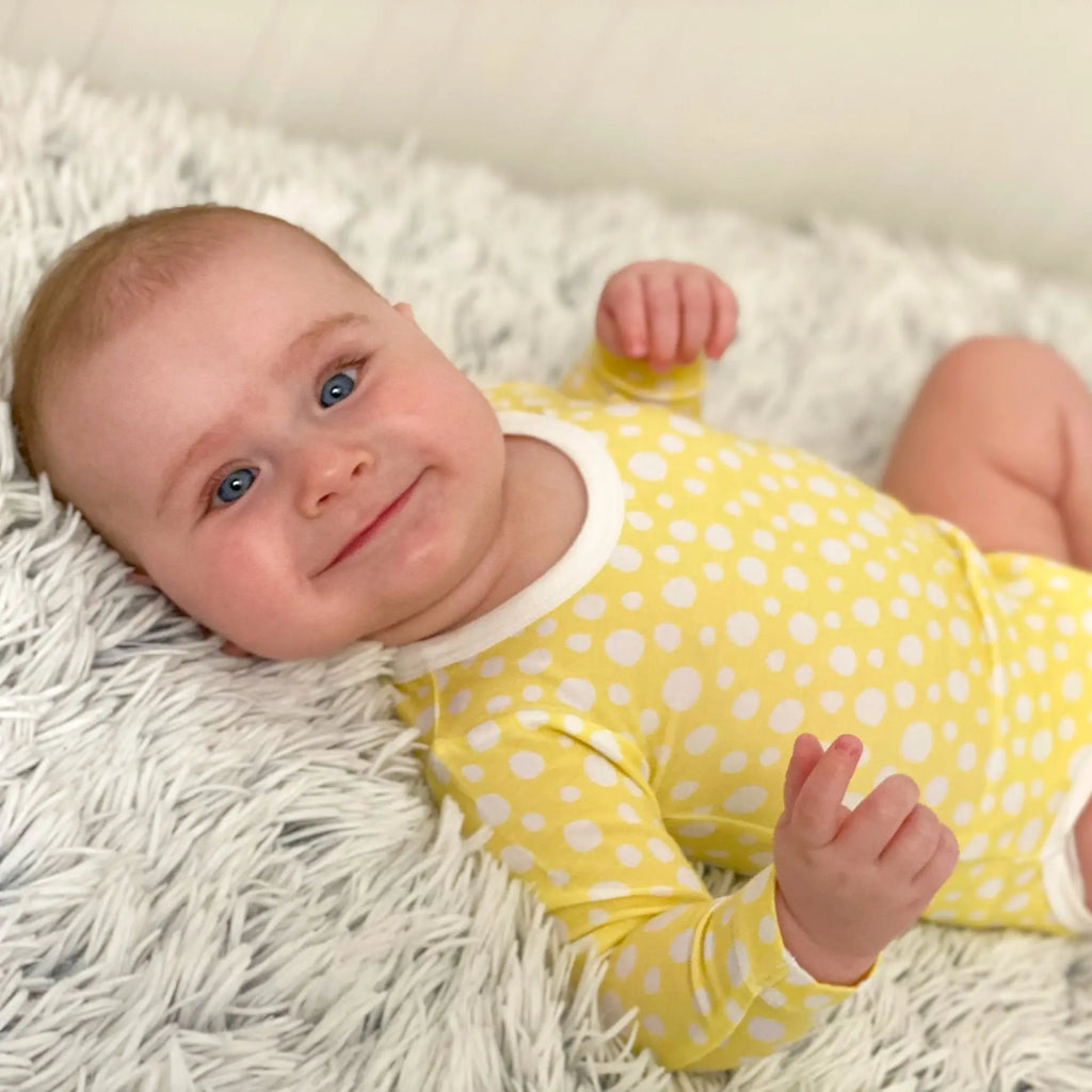 Kisfiú hanyatt fekve sárga pöttyös bambusz bodyban