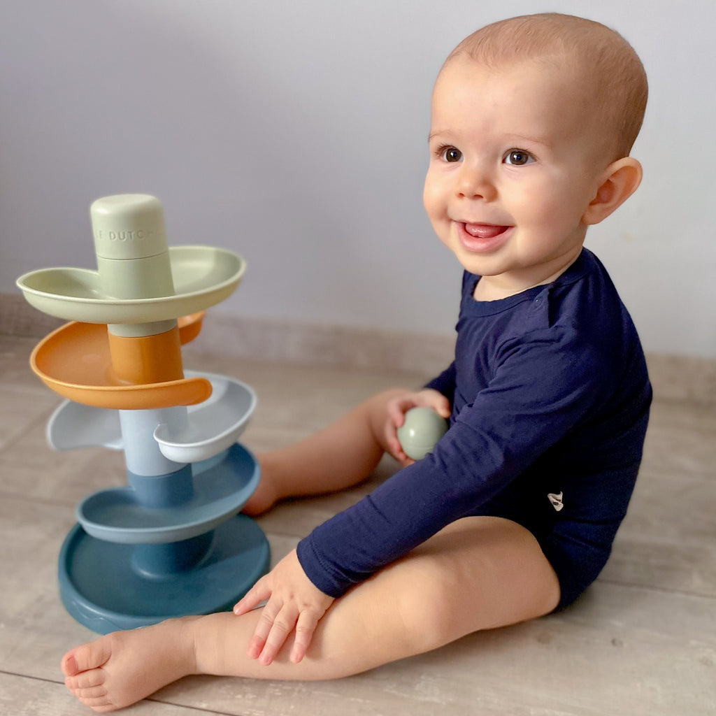 Kisfiú kék bambusz bodyban ül a földön a játékával és mosolyog